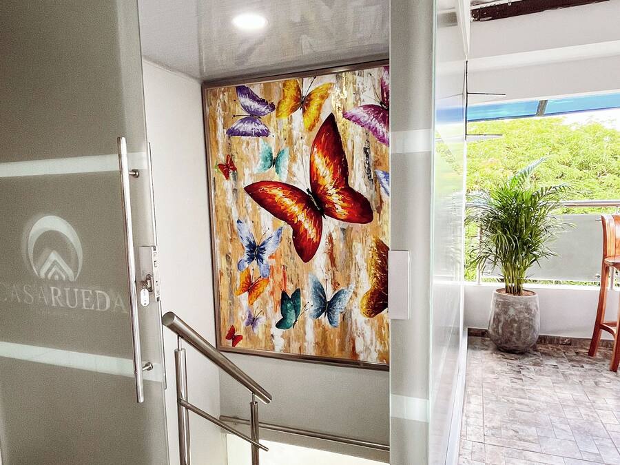 Un interior moderno con un piso de vidrio que da a una escalera, un mural de mariposas de colores y vistas al verdor exterior.