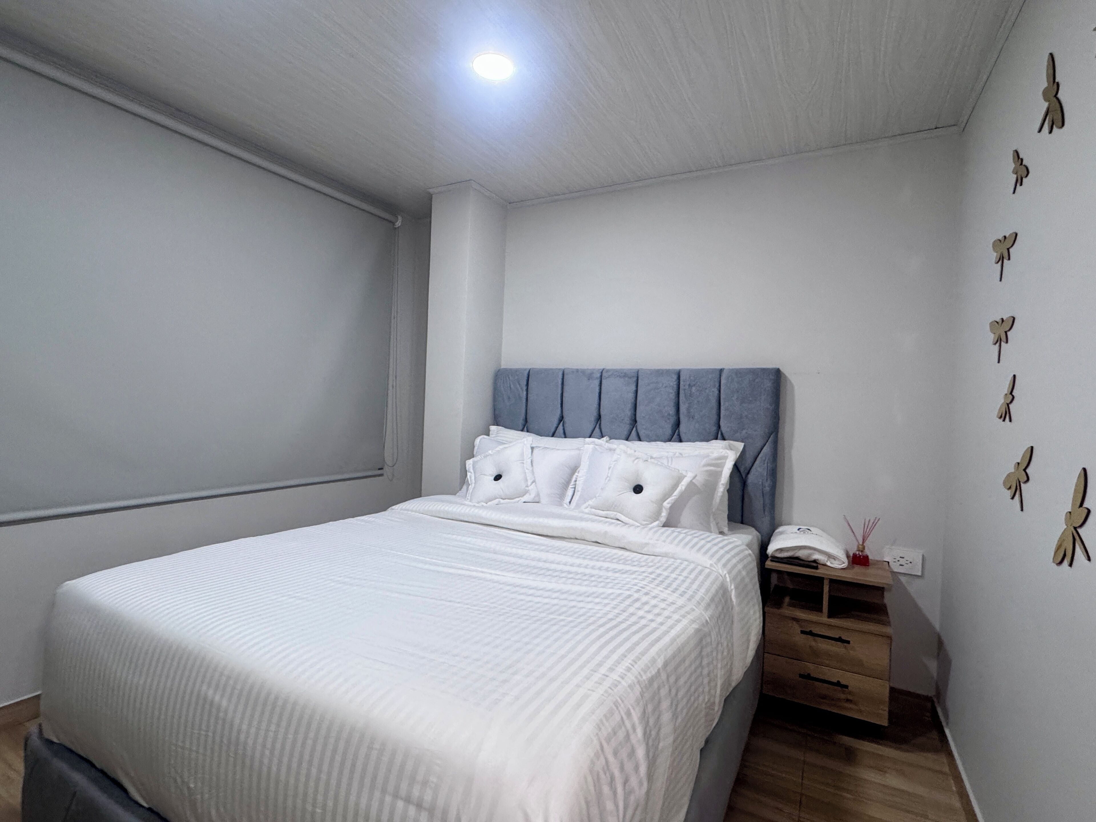 A bedroom with a bed, a bedside table, a nightstand, and a wall with butterfly decorations.