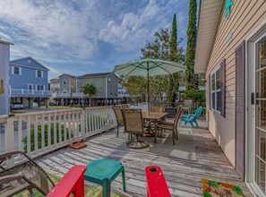 A wooden deck with outdoor furniture, a white fence, and a view of neighboring houses. - MH138 Ocean Lakes Pet Friendly Golf Cart ⛱️🏝️🩱🌊👙☀️🐚 (Myrtle Beach)