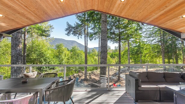 A covered outdoor area with a dining table and chairs, a sofa, and a view of a forest and mountains. - River Retreat w/ hot tub, beach & arcade/ game room (Packwood)