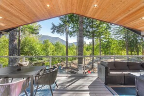 Un espace extérieur abrité comprenant une table et des chaises, un canapé, et offrant une vue sur une forêt et des montagnes.