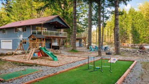 A cabin with a deck, a slide, and a play area. - River Retreat w/ hot tub, beach & arcade/ game room (Packwood)
