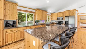 A spacious kitchen with wooden cabinets, granite countertops, and a large island with bar stools. - River Retreat w/ hot tub, beach & arcade/ game room (Packwood)