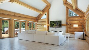 Uma sala de estar espaçosa com um amplo sofá seccional branco, vigas de madeira e uma televisão fixada na parede.