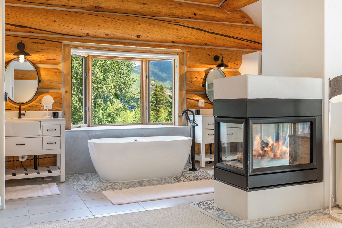 A modern bathroom with a freestanding bathtub, a fireplace, and a large window offering a view of greenery.