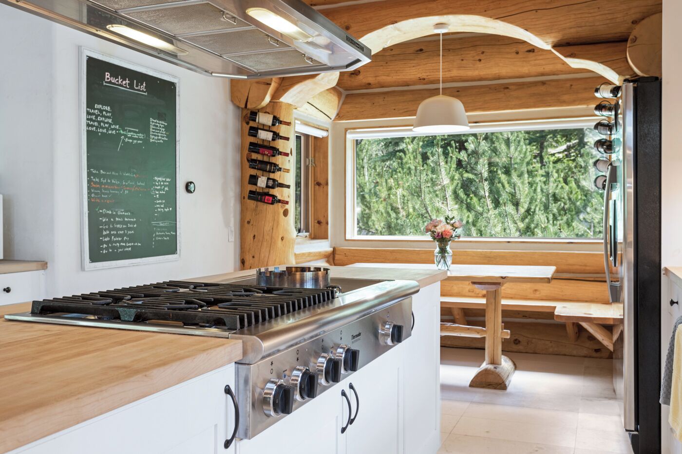 Una cocina con techo de madera, una pizarra con una lista de deseos y vistas a árboles a través de un ventanal grande.