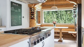 Uma cozinha com teto de madeira, uma lousa com lista de desejos e vista para árvores por uma grande janela.