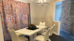 Een eetgedeelte met een witte tafel en stoelen, een kroonluchter en een gordijn met een patroon.