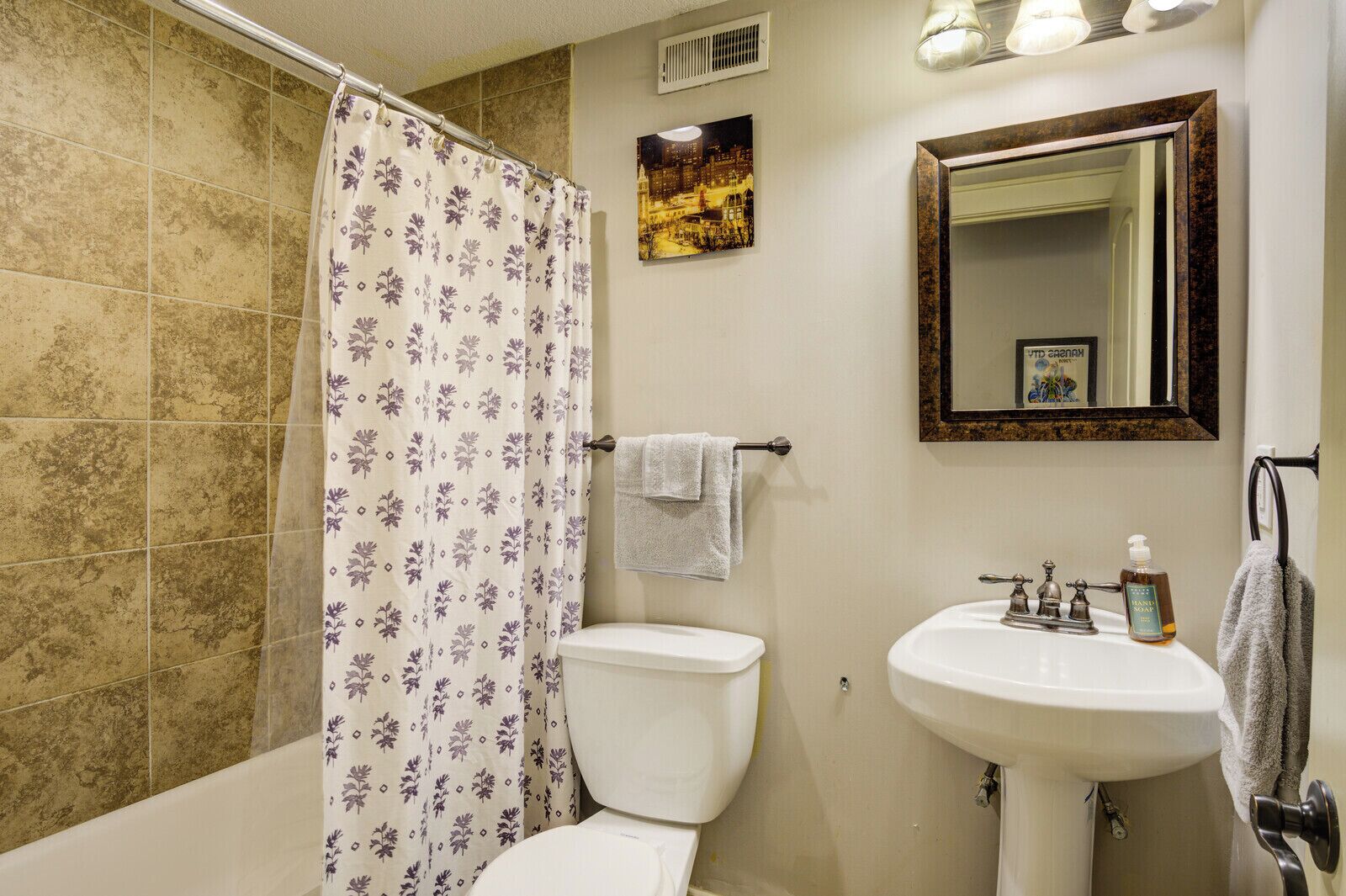 A bathroom with a shower curtain, toilet, sink, and mirror.