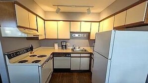 Una cocina compacta con armarios blancos, estufa, lavaplatos y refrigerador.