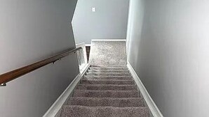Una escalera con peldaños alfombrados y barandillas de madera, que conduce a un rellano con un interruptor de luz.