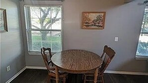 Un comedor con una mesa redonda de madera y cuatro sillas, un cuadro en la pared y una ventana con persianas.