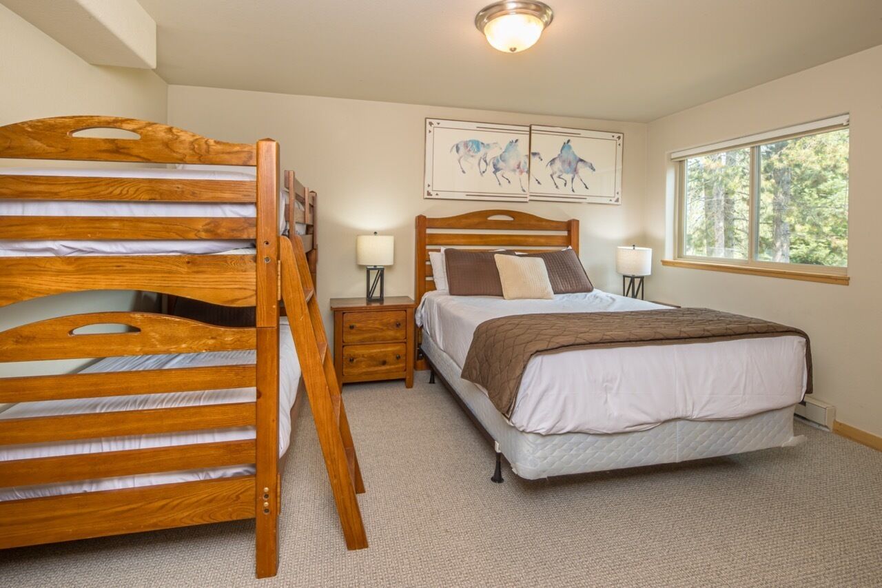 A bedroom with a wooden bunk bed, a single bed, two bedside tables, a window with a view of trees, and two wall-mounted horse paintings.