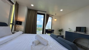 Habitación de hotel con cama, escritorio, silla, televisor y balcón con vista a la ciudad.