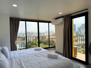 Una habitación de hotel con una cama grande, vistas a la ciudad y un equipo de aire acondicionado.