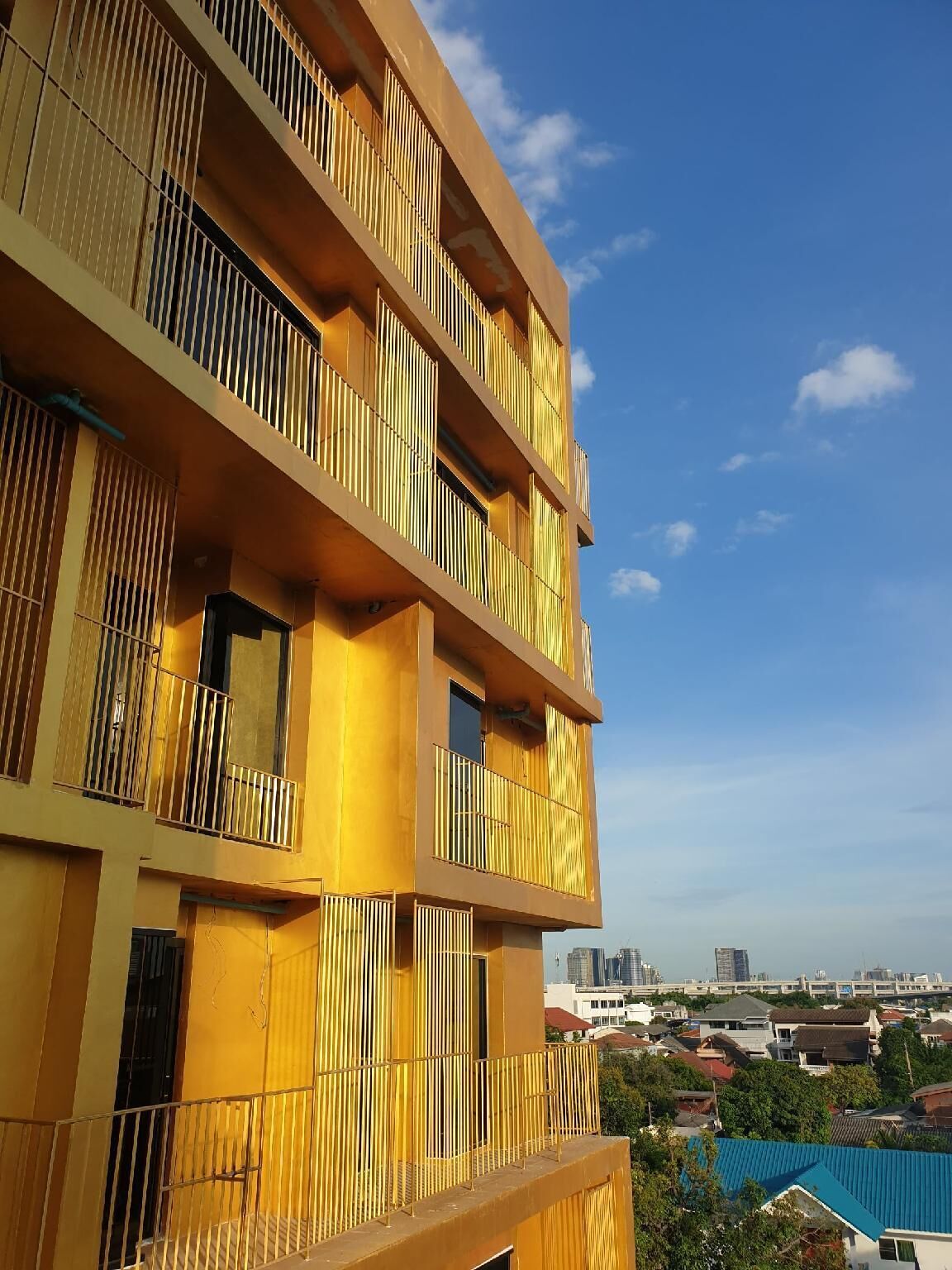 A multi-story building with balconies, a clear sky, and a distant cityscape.