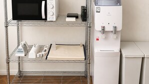 Eine Küchenzeile mit Mikrowelle, Toaster und Wasserspender auf einem Metallregal sowie ein kleiner Kühlschrank.