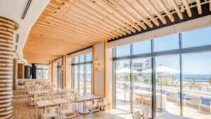 Un ristorante moderno con travi in legno al soffitto, ampie finestre e vista sulla spiaggia.