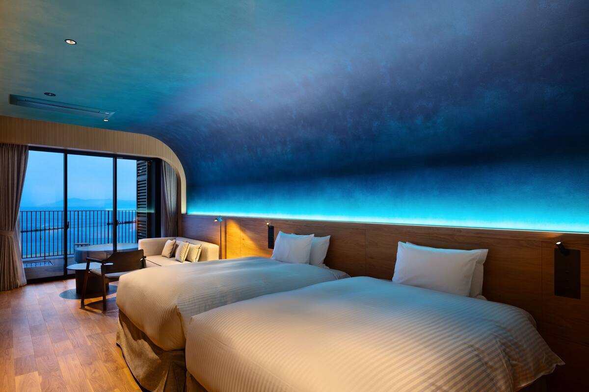 Una camera d'hotel moderna con due letti, un balcone vista mare e pavimento in legno.