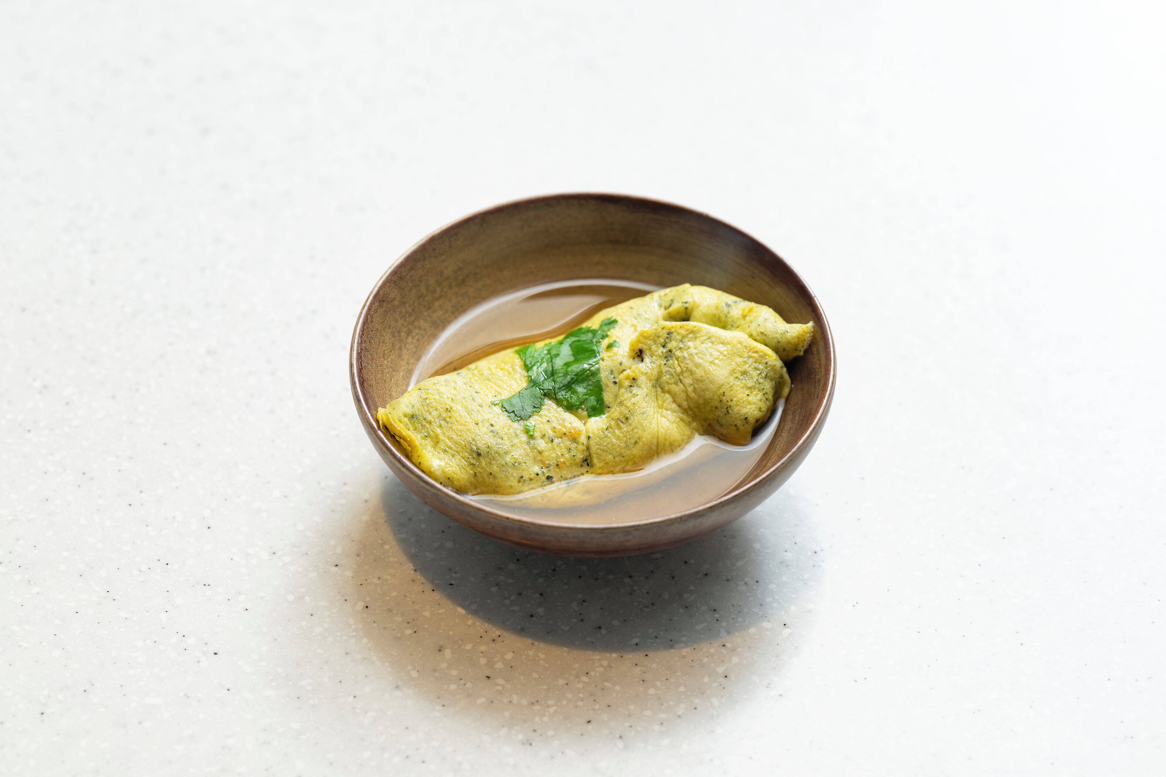 A bowl of food with a green garnish on a speckled surface.