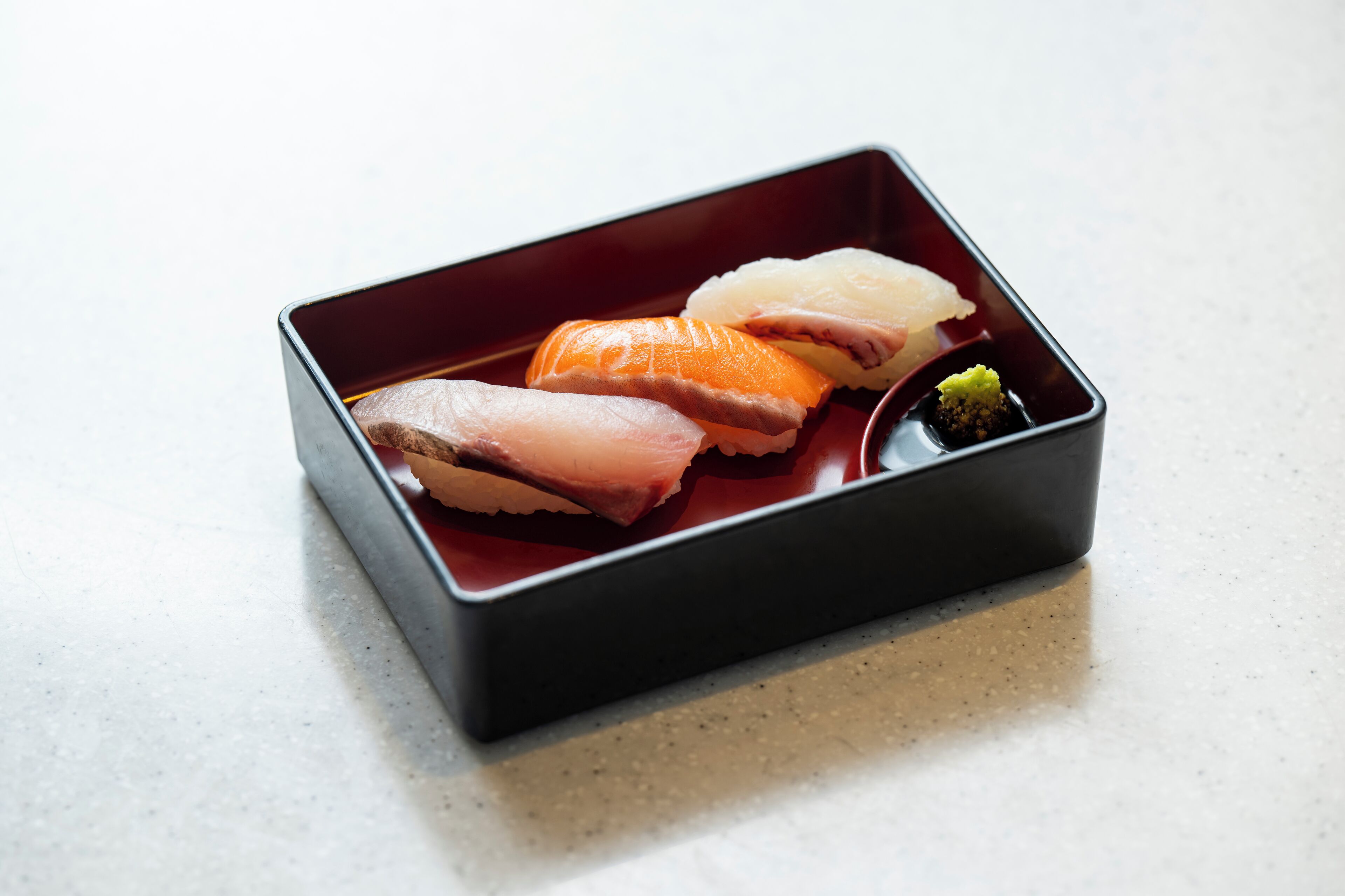 A rectangular black tray with four pieces of sushi and a small green garnish on a white surface.
