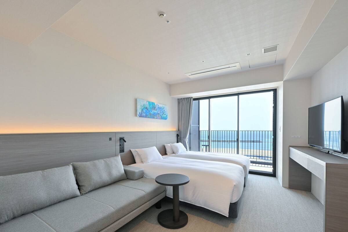 Una camera d'hotel moderna con un letto grande, un divano, una TV e un balcone con vista sul mare.