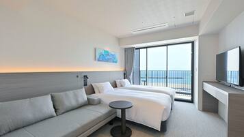 Habitación de hotel moderna con una cama grande, un sofá, un televisor y un balcón con vista al mar.