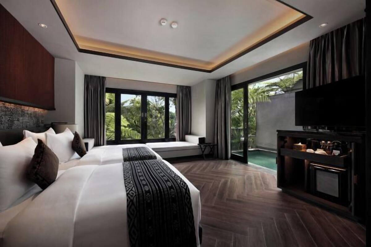 A modern hotel room with a large bed, a TV, and a balcony with a view of greenery.