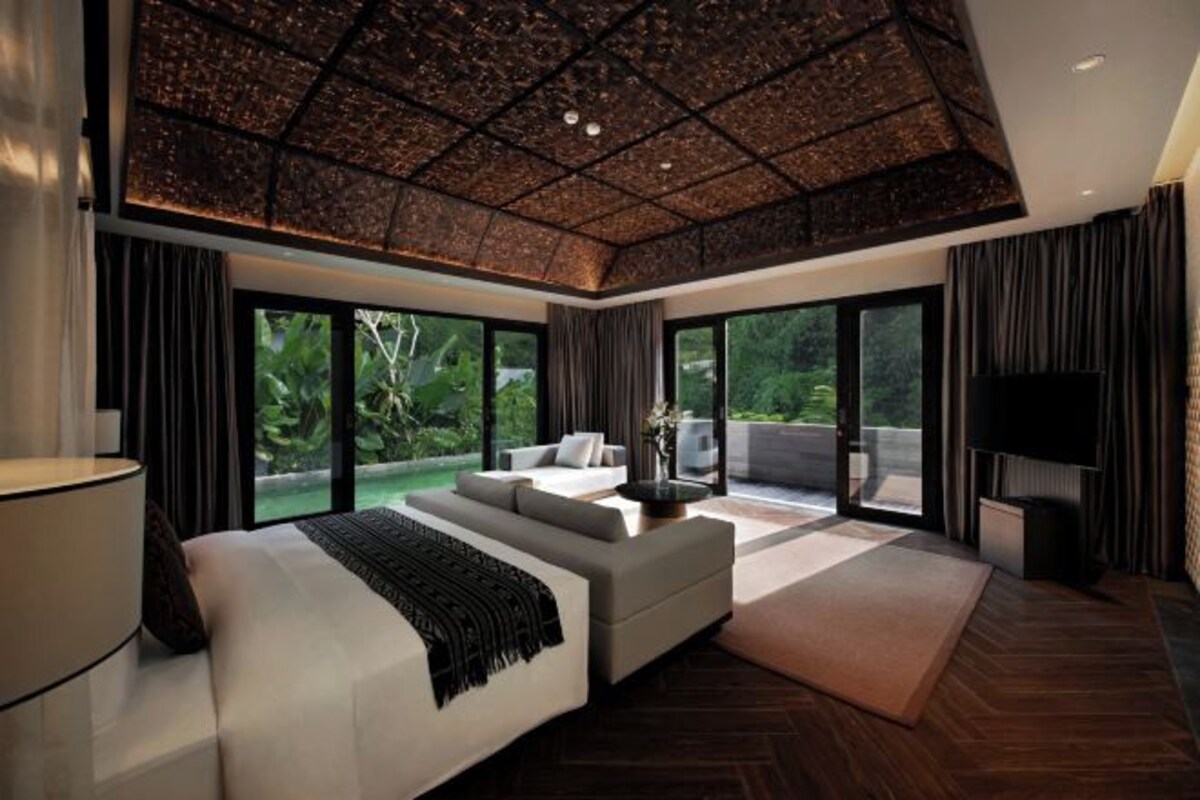 Un dormitorio moderno con una cama grande, un sofá, un televisor y un balcón con vistas a zonas verdes.