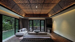 A modern bedroom with a large bed, a sofa, a coffee table, and a TV. There is a large window with a view of greenery outside. - Ayatara Resort Ubud  (Kerta)