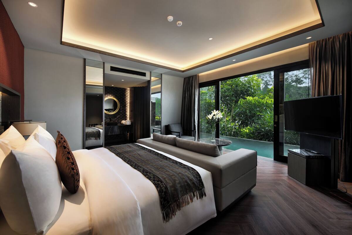A modern bedroom with a large bed, a TV, and a view of a pool.