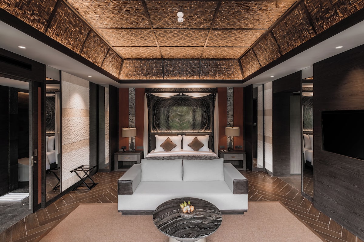 A modern hotel room with a large bed, bedside tables, a flat-screen TV, and a decorative ceiling.