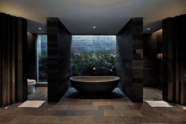 Une salle de bain moderne avec une baignoire sur pieds, des murs en pierre et une vue sur la verdure environnante.