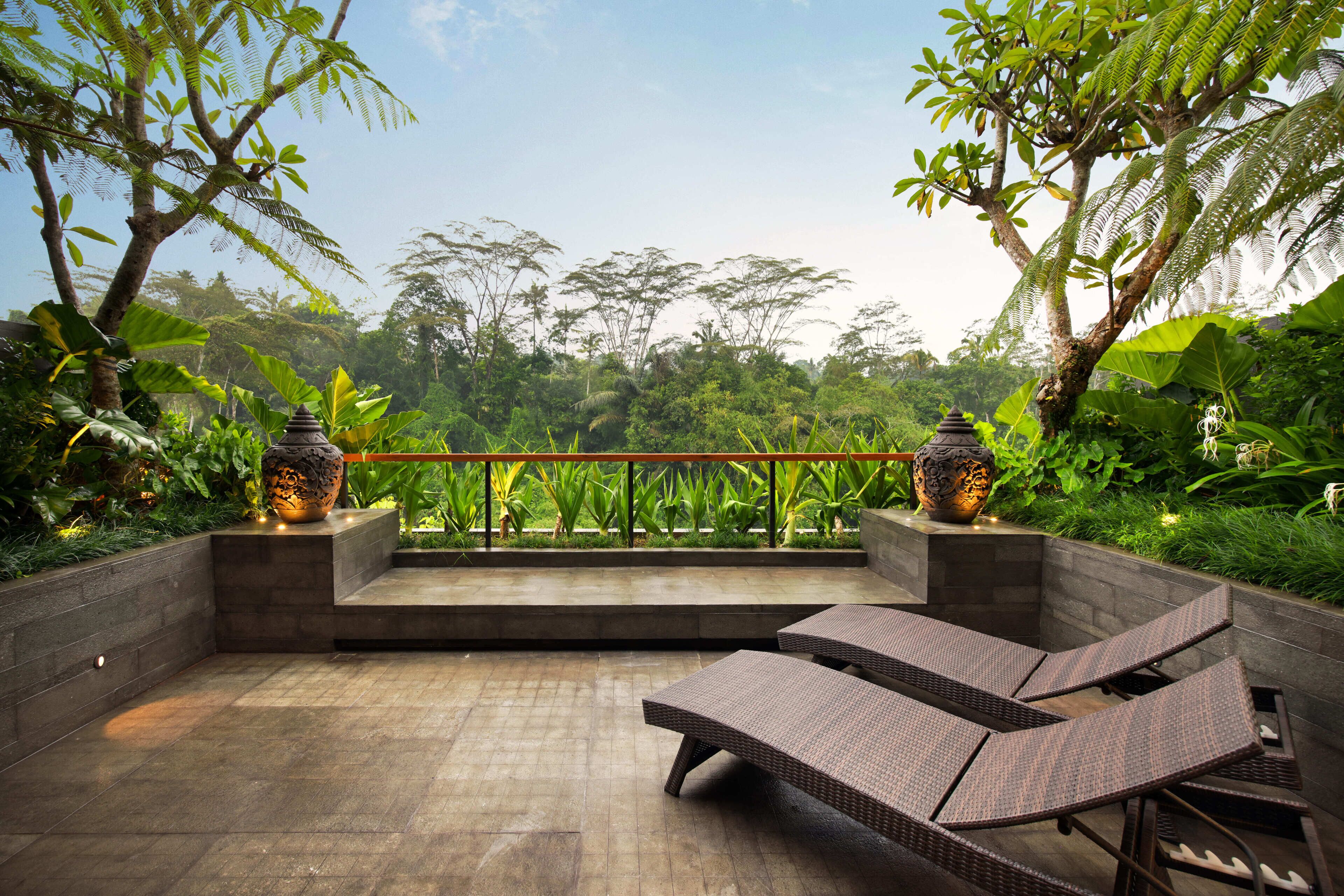 Un patio con dos sillones, un jarrón decorativo y una baranda con vista a un jardín exuberante.