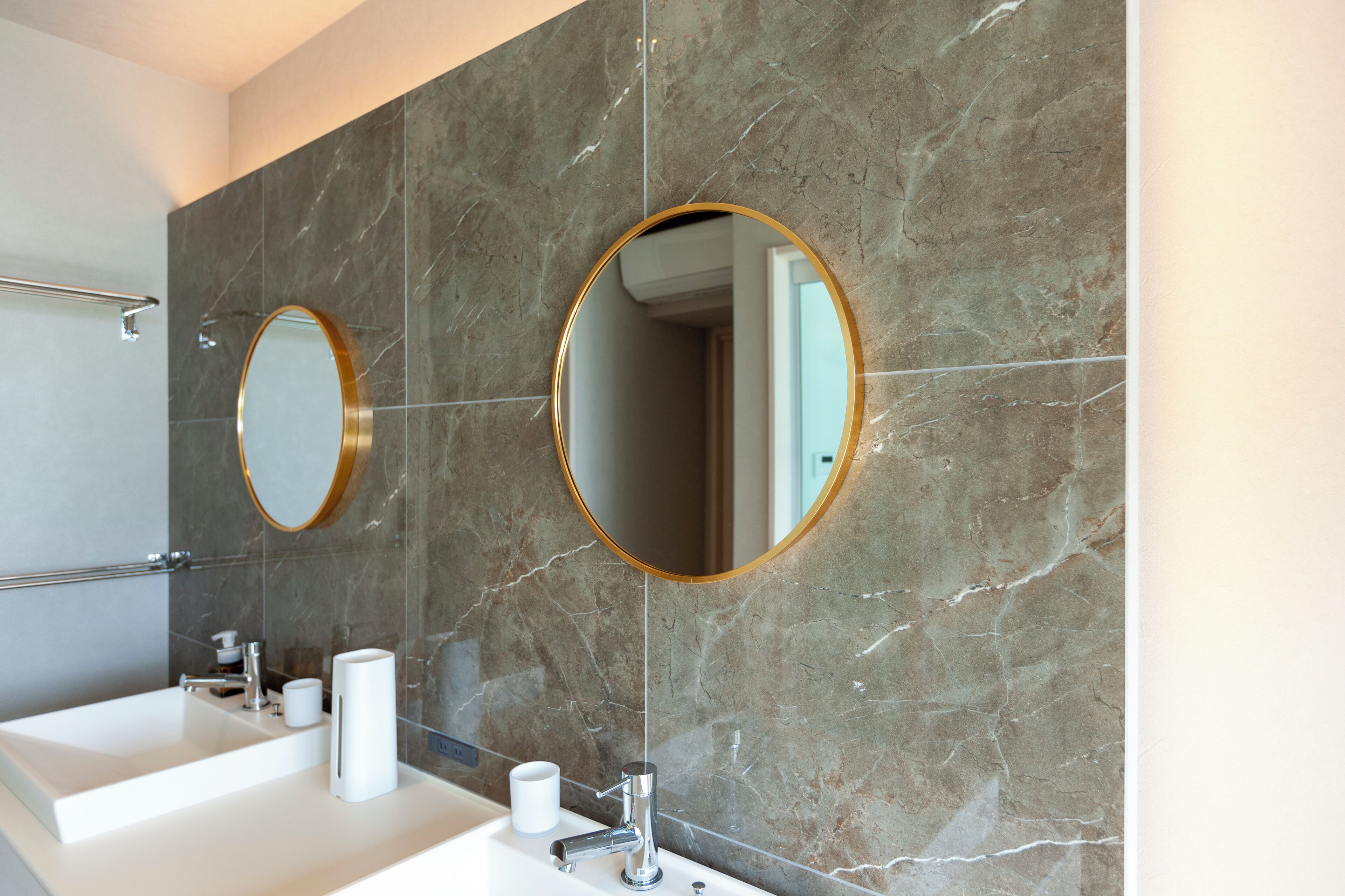 Une salle de bain avec un lavabo blanc, deux miroirs ronds dotés de cadres dorés et un mur en marbre.