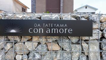 Un muro di pietra con un cancello in metallo e un cartello che recita 'DA TATEYAMA con amore'.