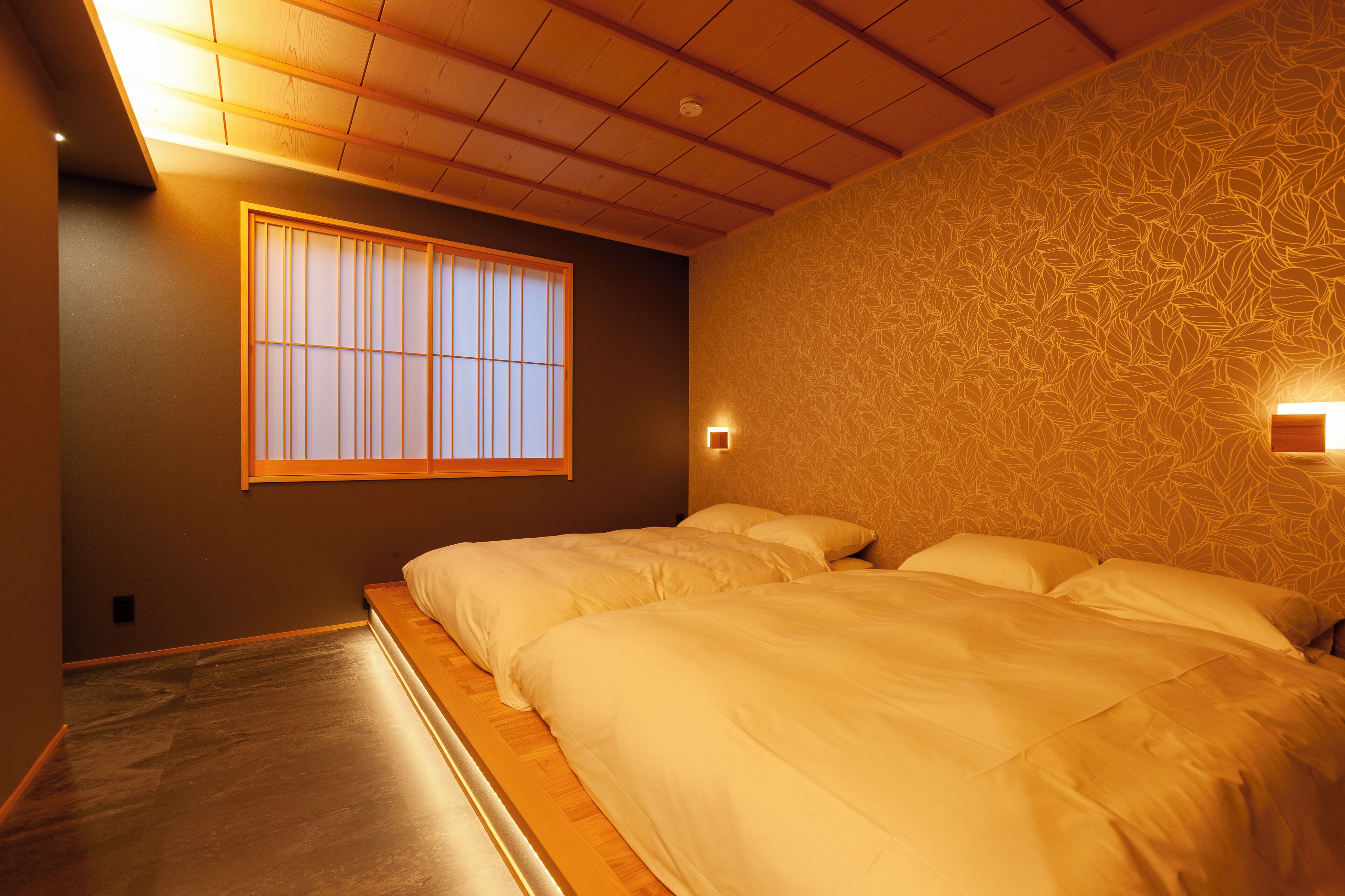 A room with a low ceiling, wooden beams, a large window with vertical blinds, and a bed with white bedding.