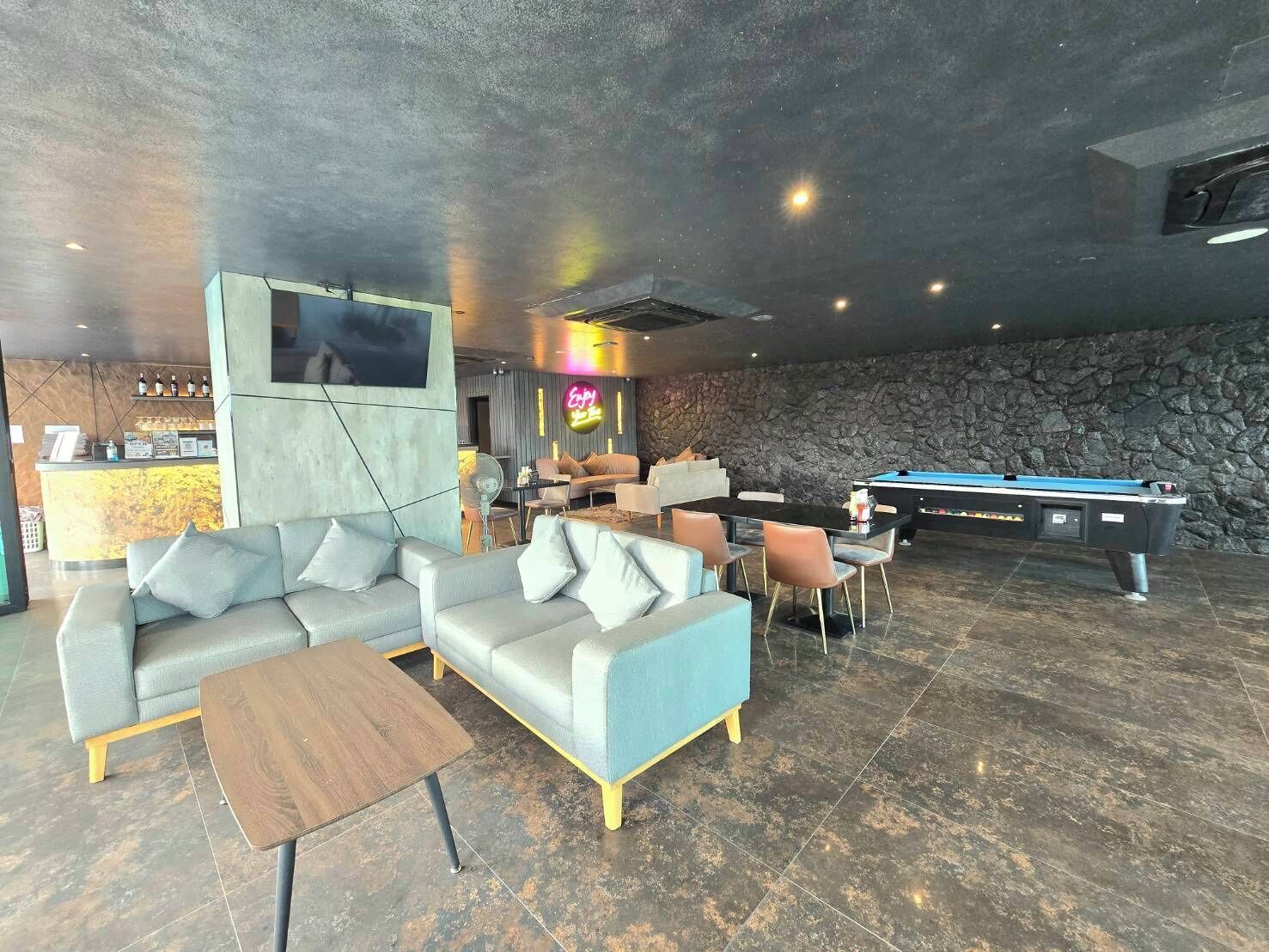 A modern lounge area with a pool table, sofas, and a bar area with a neon sign.