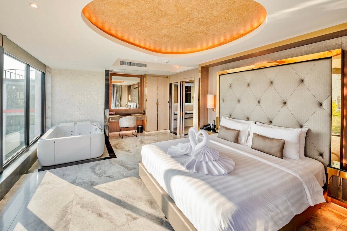 A modern hotel room with a large bed, a separate bathroom, a jacuzzi, and a view of the city.