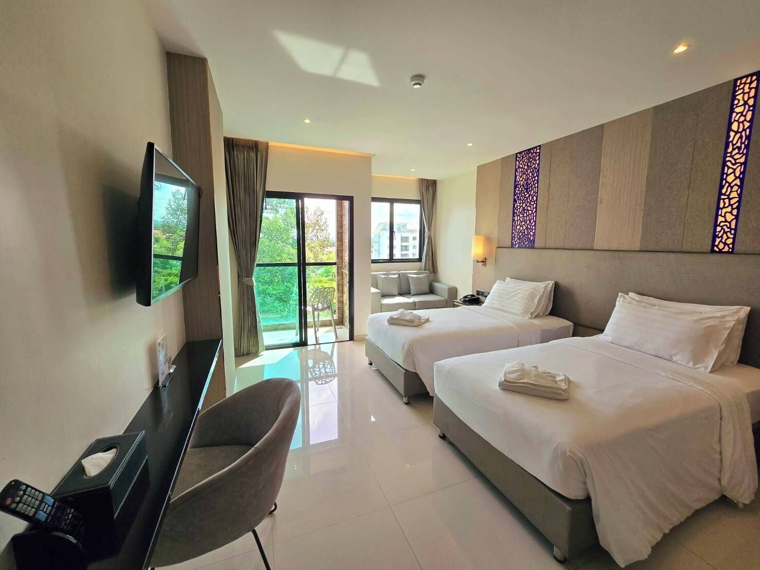 Habitación de hotel con dos camas, televisión, escritorio con silla y balcón con vistas a zonas verdes.
