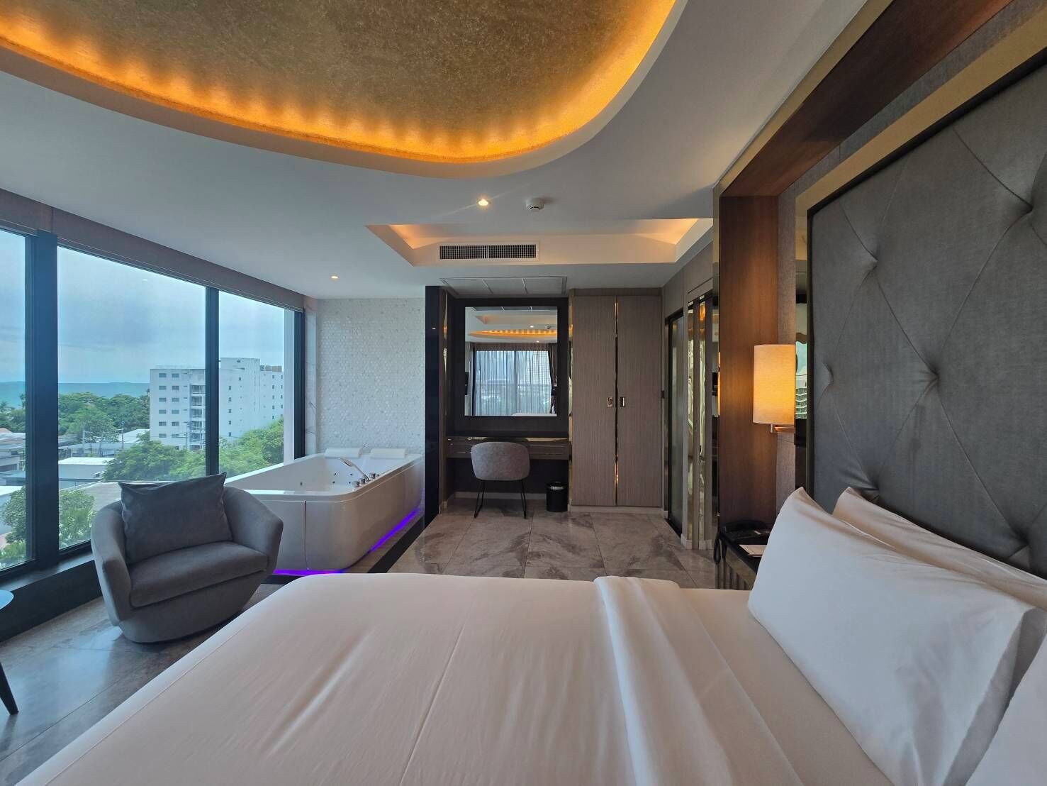 A modern hotel room with a large bed, a seating area with a chair, a desk, and a bathtub.