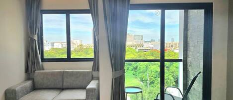 Una habitación de hotel moderna con un sofá gris, una cama y ventanas amplias con vistas a la ciudad.