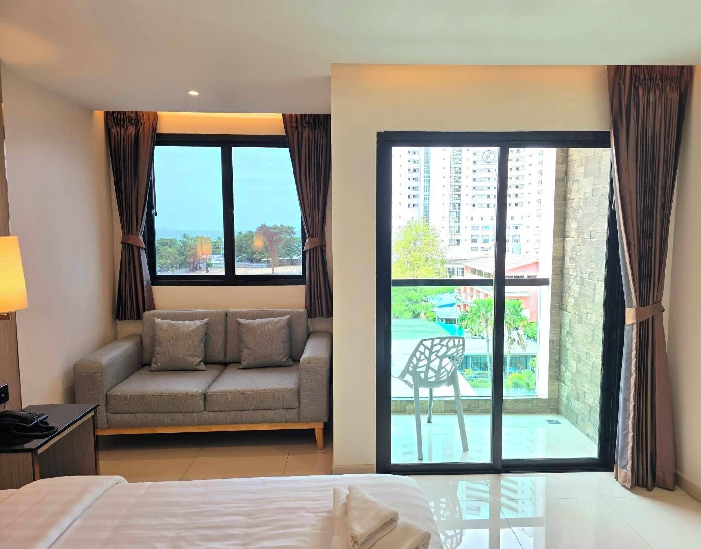Una habitación de hotel con cama, sofá, escritorio y un ventanal con cortinas.