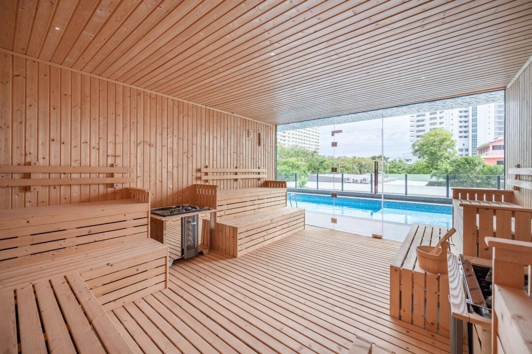 Een houten sauna met banken en een saunatableau, een zwembad en uitzicht op gebouwen en bomen.