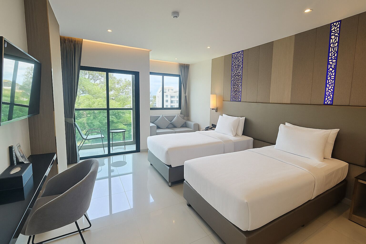 A modern hotel room with two beds, a desk, a chair, and a balcony with a view of greenery.
