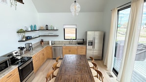 A modern kitchen with a central wooden table, built-in appliances, and a large window offering a view of the outdoors. - Bryce, Zion National and State Park Retreat (Hatch)