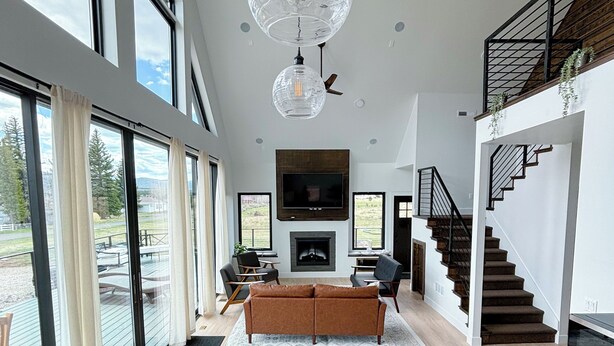 A spacious living room with a wooden dining table, large windows, a fireplace, and a staircase. - Bryce, Zion National and State Park Retreat (Hatch)