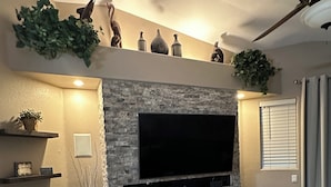 A living room with a flat-screen TV, stone accent wall, and a ceiling fan. - Beautiful home on Golf Course in gated community centrally located in Phoenix.  (Phoenix)