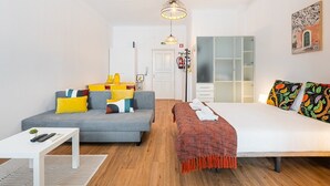 A modern hotel room with a grey sofa, a white bed, and a small table with a plant. - GuestReady - Peaceful home with a private patio (Porto)