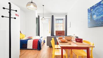 Quarto de hotel moderno com cama, área de jantar com mesa e cadeiras, um quadro na parede e uma placa indicando que o quarto está pronto para hóspedes.